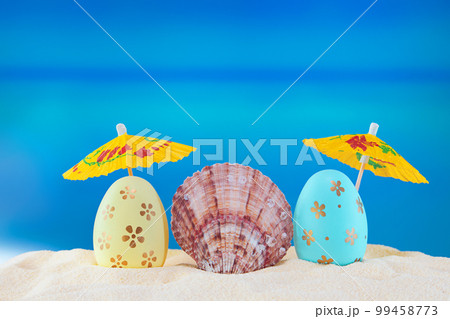 Happy easter. Yellow and blue eggs with conch shell under umbrellas on sandy beach of the sea or ocean. Holiday postcard in hot country. Travel, spring, summer. Copy space Happy easter. Yellow and blue eggs with conch shell under umbrellas on sandy beach of the sea or ocean. Holiday postcard in hot country. Travel, spring, summer. Copy space 99458773