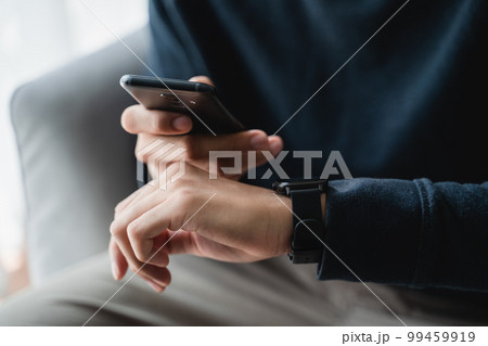 Man using smartphone and smartwatch for tracking activity on sofa in living room at home, wireless connection between the watch and mobile phone. Man using smartphone and smartwatch for tracking activity on sofa in living room at home, wireless connection between the watch and mobile phone. 99459919