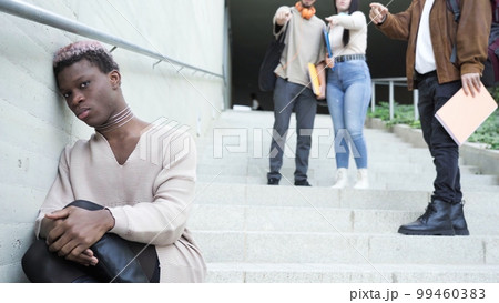 Classmates bullying sad black transgender man on stairs 99460383
