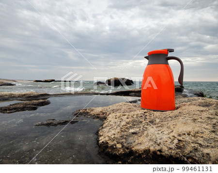 Orange thermos on the shore. Orange thermos on the shore. 99461131