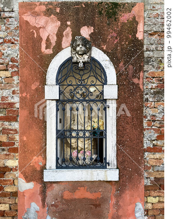 outdoor statue of Madonna behind bars in wall 99462002