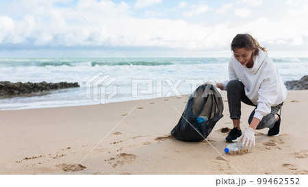 Young female volunteer picking bottles into plastic bag black for cleaning beach in morning time, panorama, free space Young female volunteer picking bottles into plastic bag black for cleaning beach in morning time, panorama, free space 99462552