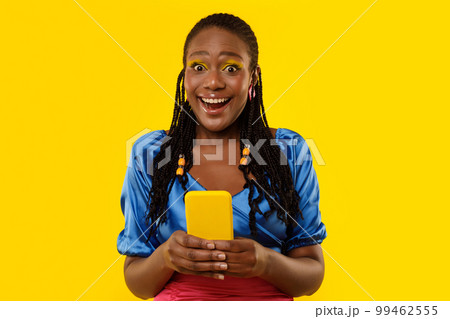 Excited African American Female Holding Smartphone Standing On Yellow Background Excited African American Female Holding Smartphone Standing On Yellow Background 99462555