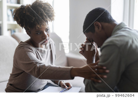 Friendly black woman therapist consoling upset young man 99462604