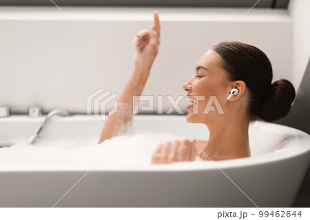 Female Listening Music Wearing Earbuds Relaxing In Bath At Home Female Listening Music Wearing Earbuds Relaxing In Bath At Home 99462644
