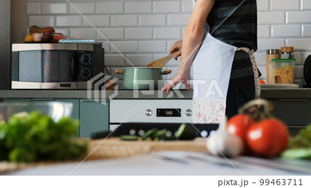 Man in apron cooking soup in the kitchen, stirring something in a pot 99463711