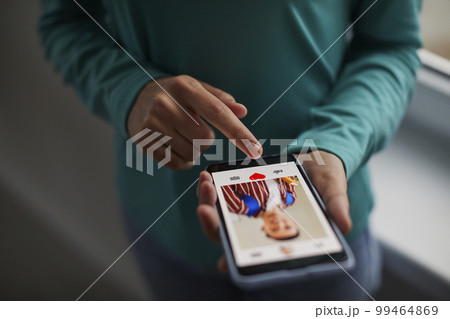 Close-up of person using mobile phone for internet use. Young man holds his finger on the smartphone screen and puts like on photo portrait on social networks. 99464869