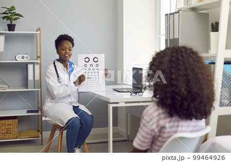 Female optometrist examines vision of child girl patient using vision chart in hospital office. 99464926