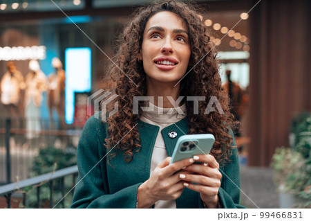 Beautiful young woman in green coat using her cellphone in the city 99466831