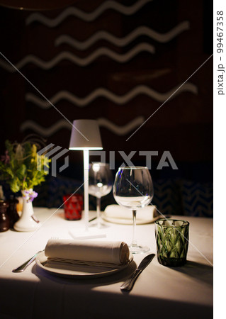 a table with a white tablecloth, glasses, crockery and decor in dark restaurant a table with a white tablecloth, glasses, crockery and decor in dark restaurant 99467358