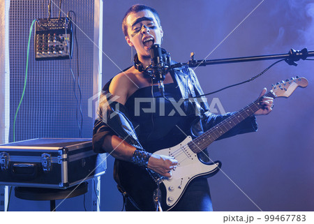 Talented guitarist singing alternative rock at microphone, playing electric guitar in studio. Doing live heavy metal performance and feeling ecstatic, screaming loud and enjoying solo concert. 99467783
