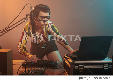 Musical performer using turntables to mix techno music, producing sounds at dj mixer with electronics and bass key. Woman working as artist doing remix performance at nightclub in studio. 99467807