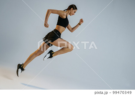 Determined sporty woman running in Mid-Air exercising during cardio workout over studio background 99470349