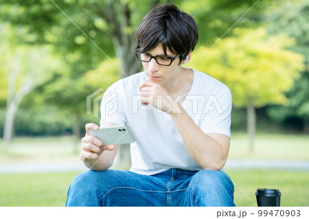 新緑の公園でスマホ動画を観る眼鏡の男性 99470903