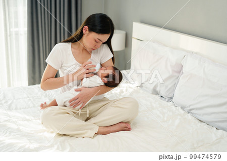 mother feeding milk bottle to her newborn baby on bed mother feeding milk bottle to her newborn baby on bed 99474579