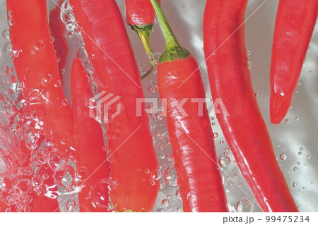 Close-up view of the red chilli peppers in water background. Texture of cooling vegeteble drink with macro bubbles on the white wall. Flat design. Horizontal image. Splashing liquid and red chilli 99475234