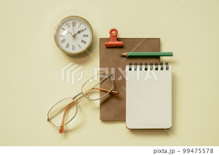 Notepad, diary, clock, eyeglasses, pencil, clip on yellow desk background. flay lay, top view, copy space 99475578