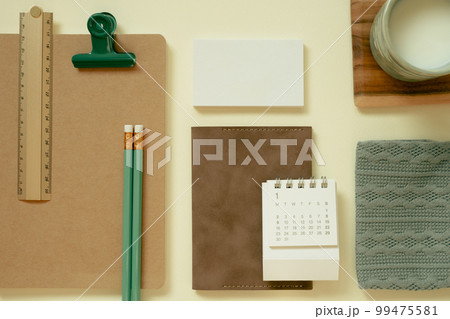 Office supply, stationery. Brown notebook, calendar, cup of milk, pencil, ruler, clip, pouch, memo pad on yellow desk background. flat lay, top view Office supply, stationery. Brown notebook, calendar, cup of milk, pencil, ruler, clip, pouch, memo pad on yellow desk background. flat lay, top view 99475581