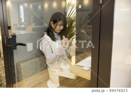 デザインオフィスの個室ブースでスマホを操作する若い女性 99476925