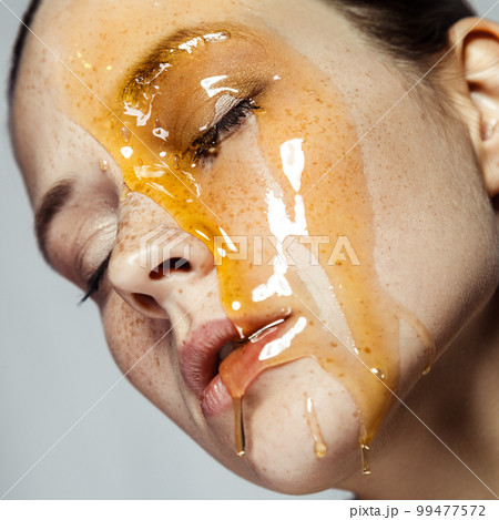 Closeup profile portrait of relaxed calm young brunette woman with freckles, standing with closed eyes, doing skin care procedures with honey mask. Indoor studio shot isolated on gray background. 99477572