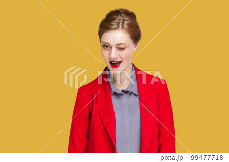 Portrait of positive flirting woman with red lips blinking her eyes with pleasure having happy expression, wearing red jacket. Indoor studio shot isolated on yellow background. Portrait of positive flirting woman with red lips blinking her eyes with pleasure having happy expression, wearing red jacket. Indoor studio shot isolated on yellow background. 99477718