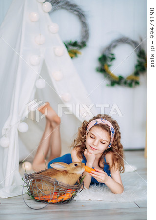 cute little girl laying on the floor and feeding rabbit carrot while learning to take care of animal cute little girl laying on the floor and feeding rabbit carrot while learning to take care of animal 99478190