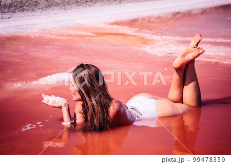 Young woman with long hair in pink salty lake with crystals of salt. Extremely salty pink lake, colored by microalgae with crystalline salt depositions. Spa, beauty and health care concept. 99478359