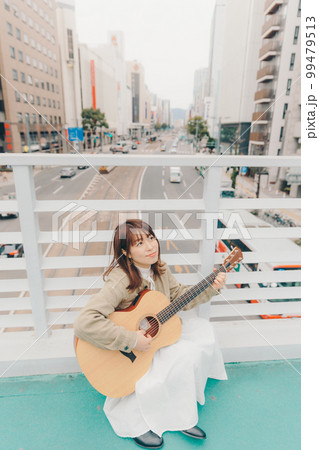 街バックにギターを持った女性の写真 99479513
