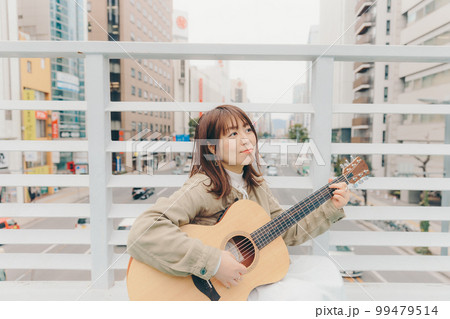 街バックにギターを持った女性の写真 街バックにギターを持った女性の写真 99479514