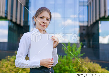 Elegant caucasian business woman in formal wear holds paper documents in her Elegant caucasian business woman in formal wear holds paper documents in her 99482220