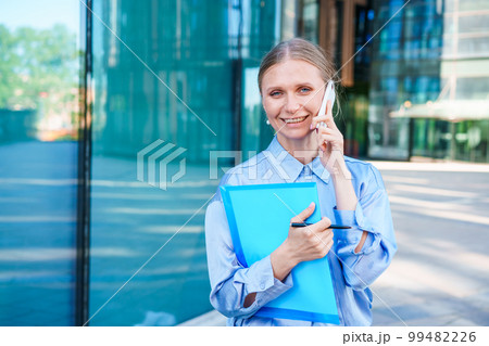 Business woman smiling happy talking on smartphone in city holding notepad 99482226