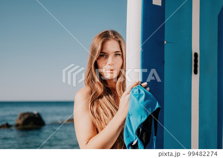 Woman sea sup. Close up portrait of happy young caucasian woman with long hair looking at camera and smiling. Cute woman portrait in a blue bikini posing on sup board in the sea Woman sea sup. Close up portrait of happy young caucasian woman with long hair looking at camera and smiling. Cute woman portrait in a blue bikini posing on sup board in the sea 99482274