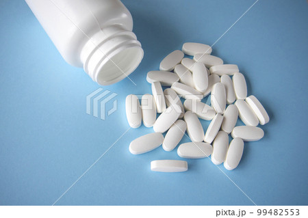 Oval white pills spilled out of the jar on a blue background. 99482553