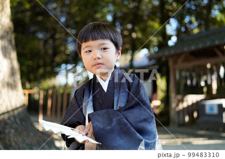 和服姿で七五三のお宮参りに来た5歳児が神社の境内で穏やかな眼差しでこちらを見つめている図（ハイキー） 99483310