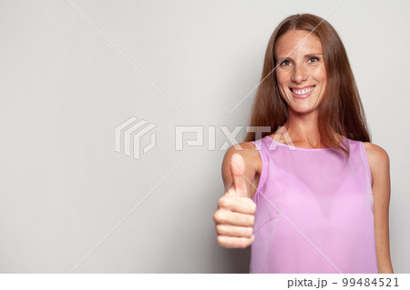 Smiling mature model woman with thumb up like gesture against white studio wall 99484521