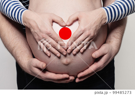 Japanese family concept. Man embracing pregnant woman belly and heart with flag Japanese family concept. Man embracing pregnant woman belly and heart with flag 99485273