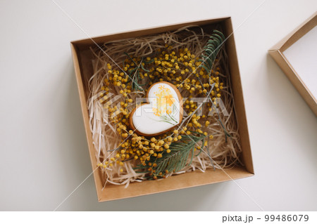 Easter gingerbread cookie in shape of a heart in a gift box with colorful yellow mimosa flowers. Eastet, Spring, April card or banner. Top view Easter gingerbread cookie in shape of a heart in a gift box with colorful yellow mimosa flowers. Eastet, Spring, April card or banner. Top view 99486079