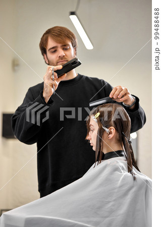 Professional male hairdresser cutting female hair in salon 99488488