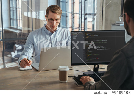 Two IT specialists co-working at office, working on new product Two IT specialists co-working at office, working on new product 99489408