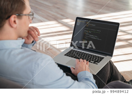 Cropped shot oof coder sitting with laptop on knees 99489412