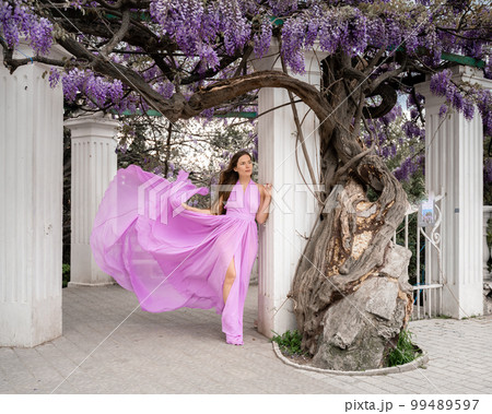 Woman wisteria purple dress. Thoughtful happy mature woman in purple dress surrounded by chinese wisteria Woman wisteria purple dress. Thoughtful happy mature woman in purple dress surrounded by chinese wisteria 99489597