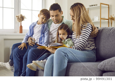 Young family reading book sitting on sofa in living room 99491301