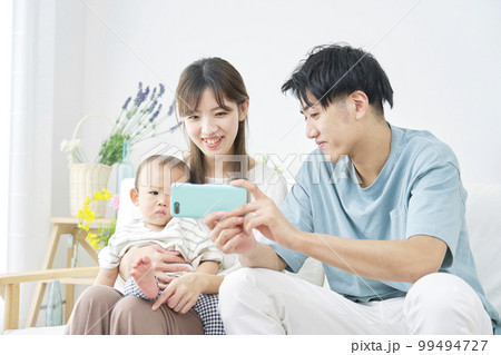 家で赤ちゃんとスマホを見る両親 家で赤ちゃんとスマホを見る両親 99494727