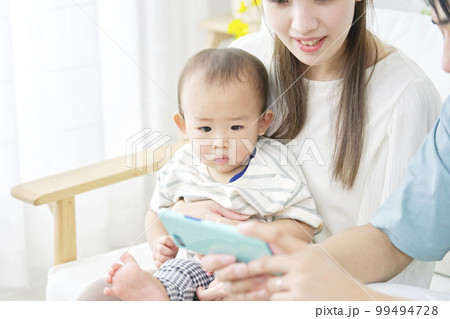 家で赤ちゃんとスマホを見る両親 家で赤ちゃんとスマホを見る両親 99494728