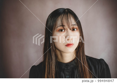 薄いピンクの背景と黒いワンピースの女性ポートレート 99494847