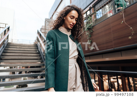 Portrait of young woman in green coat with curly hair in the city Portrait of young woman in green coat with curly hair in the city 99497108