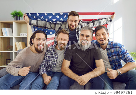 Group of men with American flag sitting on couch and watching soccer match on TV 99497861