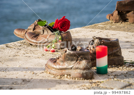Shoes on the Danube Bank, Budapest, Hungary. Memorial to the Hungarian Jews, the victims of the Holocaust executed along this riverbank during WWII. Red rose and candle. Close-up. 99497862