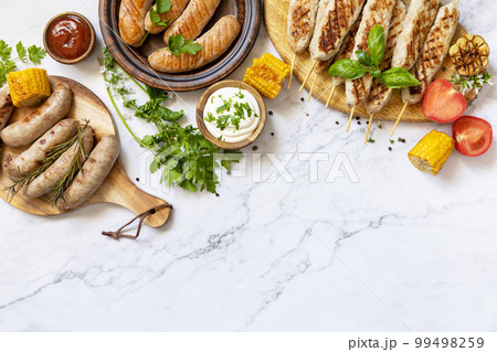 Grill food menu. Various bbq grilled sausages with fresh herbs and spices on marble tabletop. Summer party food. View from above. Copy space. Grill food menu. Various bbq grilled sausages with fresh herbs and spices on marble tabletop. Summer party food. View from above. Copy space. 99498259