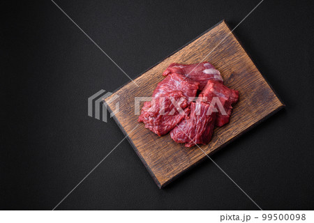 Raw beef cut into several pieces on a wooden cutting board Raw beef cut into several pieces on a wooden cutting board 99500098